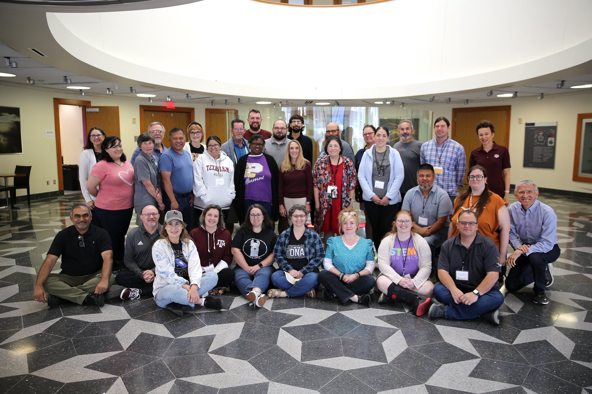 A group of teachers and instructors pose for a photo in the Mitchell Institute atrium.